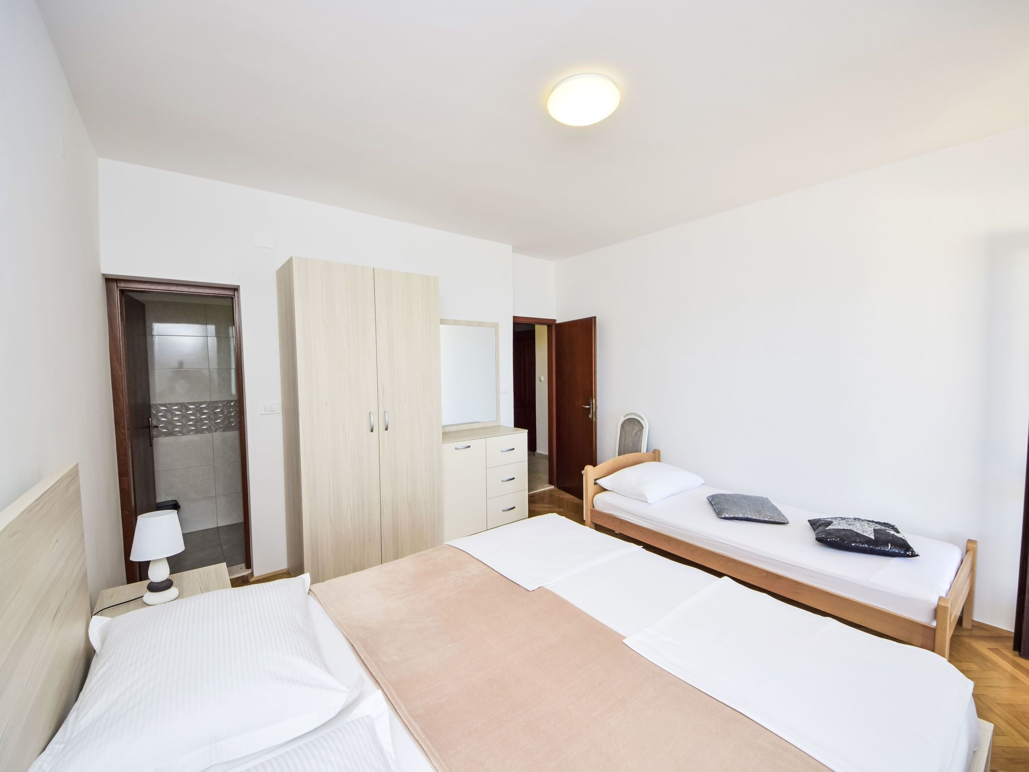Une chambre d’hôtel avec deux lits simples, une armoire, un miroir, une table de chevet avec une lampe et un luminaire au plafond.