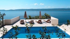 A rooftop pool with lounge chairs and umbrellas overlooking a large body of water. - Apartment Lada by Interhome (Omiš)