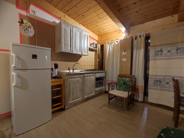 A compact kitchen with wooden cabinets, a refrigerator, a microwave, and a sink.