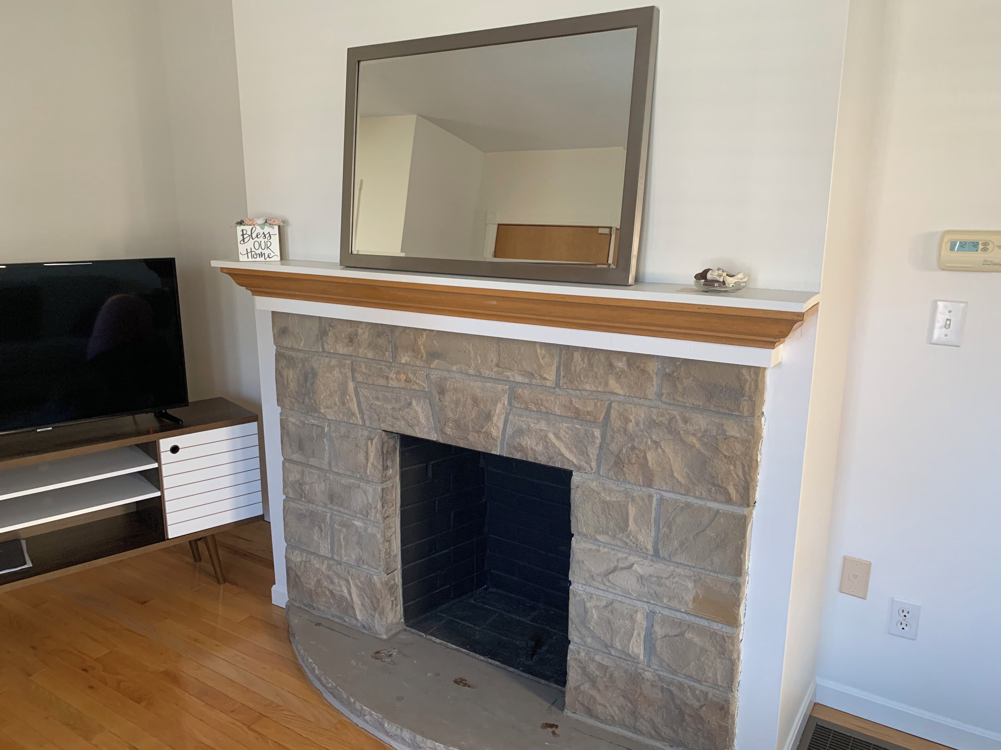A living room with a stone fireplace, a flat-screen TV, and a mirror above the fireplace.
