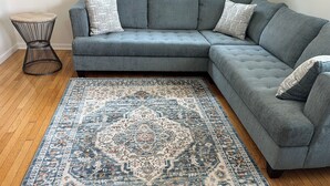 A grey sectional sofa with patterned cushions, a blue and beige area rug, and a black wireframe side table. - 2-bedroom Century house in Cleveland with modern amenities (Cleveland)