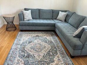 A grey sectional sofa with patterned cushions, a blue and beige area rug, and a black wireframe side table. - 2-bedroom Century house in Cleveland with modern amenities (Cleveland)