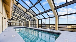 An indoor swimming pool with clear blue water, surrounded by large windows and a high ceiling.