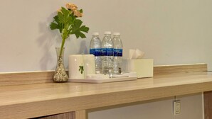 A kitchen counter with a vase of flowers, three bottles of water, a tissue box, and a coffee maker. - Keang You Boutique Hotel  (Phnom Penh)