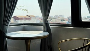 A room with a round table and a chair, a window with curtains, and a view of buildings outside. - Keang You Boutique Hotel  (Phnom Penh)