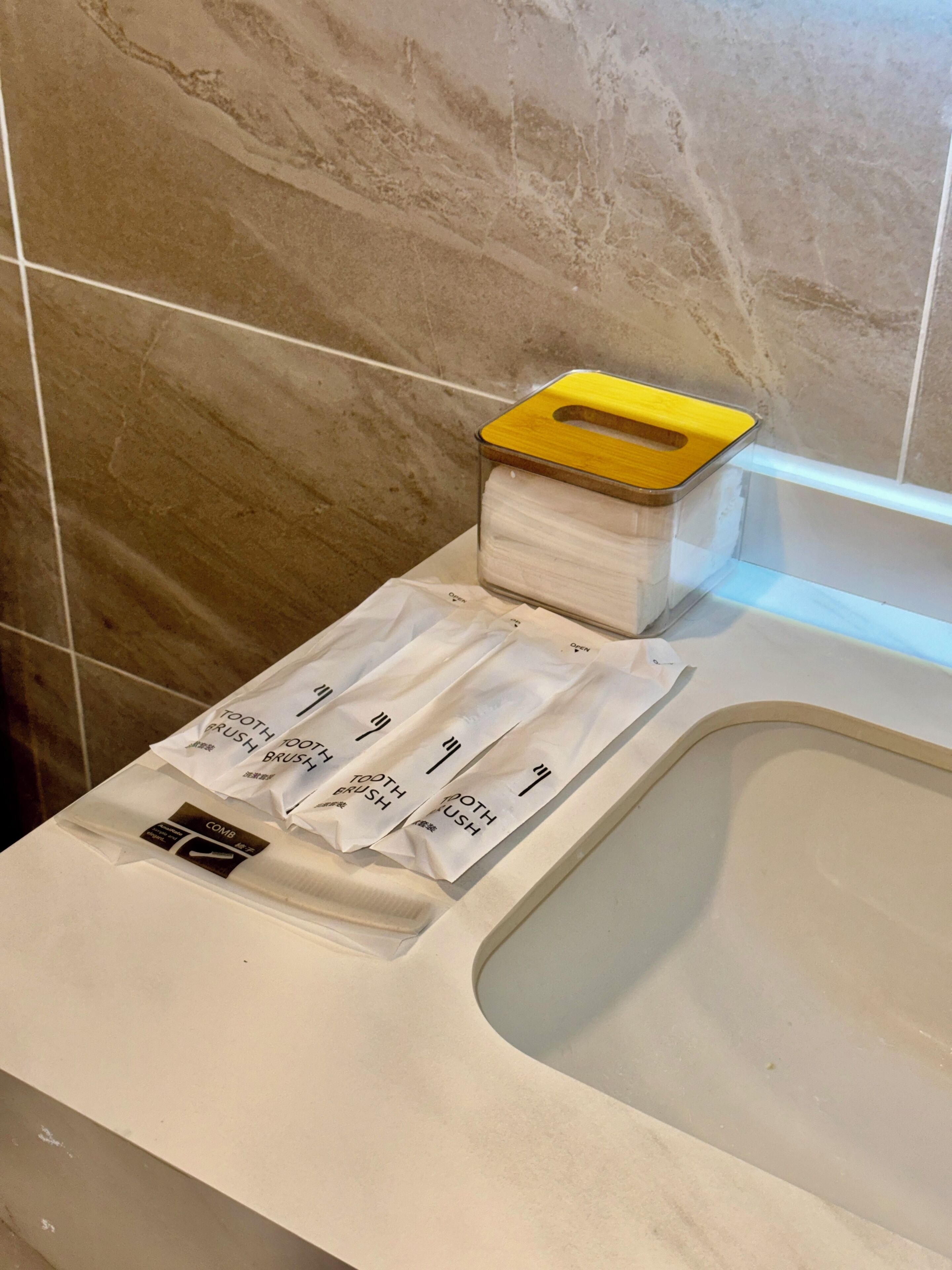 Un baño con pared de mármol, lavabo blanco y jabonera amarilla.