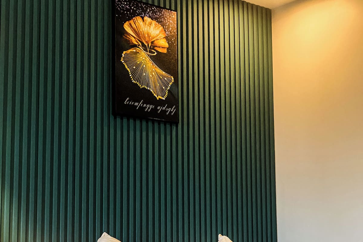 Een net opgemaakt bed met bloemenkussens, een decoratief hoofdbord en een lijstwerk erboven.