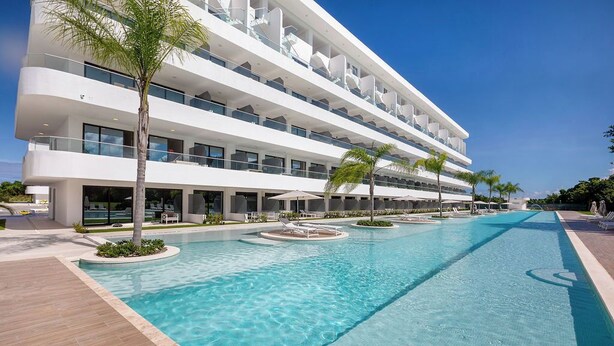 Ein modernes Hotel mit großem Außenpool, mehreren Balkonen und Palmen.