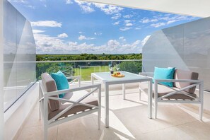 Enjoy a serene view of the lush landscape from this outdoor balcony with a glass enclosure, perfect for dining or socializing.