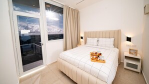 Hotellihuone, jossa on sänky, aamiaistarjotin, yöpöytä, seinään kiinnitetty lamppu ja näkymä ikkunasta.