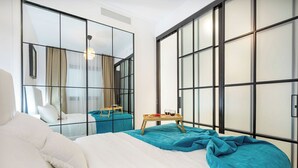 Moderni hotellihuone, jossa on suuri sänky, pieni pöytä, jonka päällä on aamiaistarjotin, ja liukuovi, joka johtaa parvekkeelle.