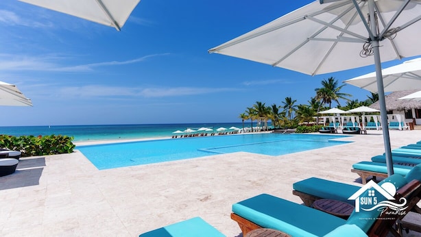 Une piscine d’hôtel avec des chaises longues et des parasols, un ciel bleu azur et une vue sur l’océan.