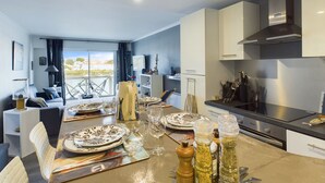 Una cocina moderna con armarios blancos, una estufa de acero inoxidable y un comedor con una mesa para dos.