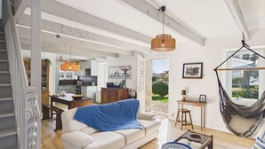 A spacious living area with a sofa, coffee table, and a hammock. A kitchen is visible in the background with modern appliances. - 50 m from the beach – House for 6 with garden (Treffiagat)