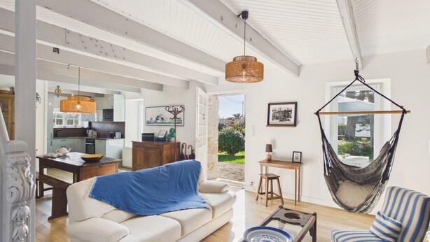 A spacious living area with a sofa, a coffee table, and a hanging chair. A kitchen is visible in the background. - 50 m from the beach – House for 6 with garden (Treffiagat)