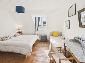 Ein Zimmer mit zwei Betten, Holzboden, einem fenster mit Vorhängen, einem Tisch mit Marmorplatte und einem Vintage-Radio.