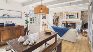 A spacious living area with a wooden dining table set for tea, a stone fireplace, and a large window overlooking the sea. - 50 m from the beach – House for 6 with garden (Treffiagat)