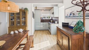 A modern kitchen with white cabinets, a wooden dining table, and a hanging light fixture. - 50 m from the beach – House for 6 with garden (Treffiagat)