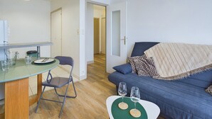 A modern living room with a blue sofa, a dining table with chairs, and a kitchen area in the background. - 100 m from the beach, 2 adults and 2 children (Fouesnant)