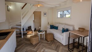 A spacious living area with a herringbone floor, a white sofa with blue cushions, a wooden dining table, and a staircase leading to another room.