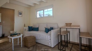 A cozy living room with a white sofa, blue cushions, a small round table, and a window with a view.