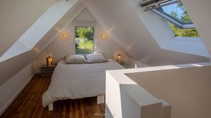 A bedroom with a sloped ceiling, skylight, and a bed with two pillows.