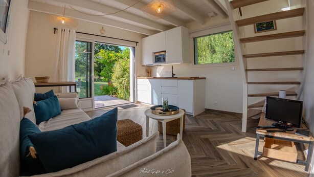 A modern living room with a sofa, a small table, and a TV. There is a kitchen area with a microwave and a window.