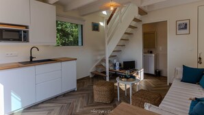 A modern kitchen with white cabinets, a microwave, and a wooden countertop. There is a staircase leading to a dining area with a table and chairs.