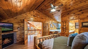 Ein gemütliches Blockhaus-Zimmer mit Kamin, einem Bett mit Kissen, einem Fernseher und einer Holzbalkendecke.