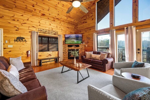Interior acogedor de una cabaña con techo de madera, chimenea, sofá, mesa de centro y televisor.