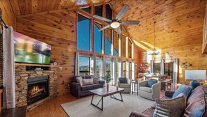 Ein gemütliches Blockhaushaus-Interieur mit Kamin aus Stein, bequemen Sitzgelegenheiten, einem Fernseher und einer Kaffeebar.