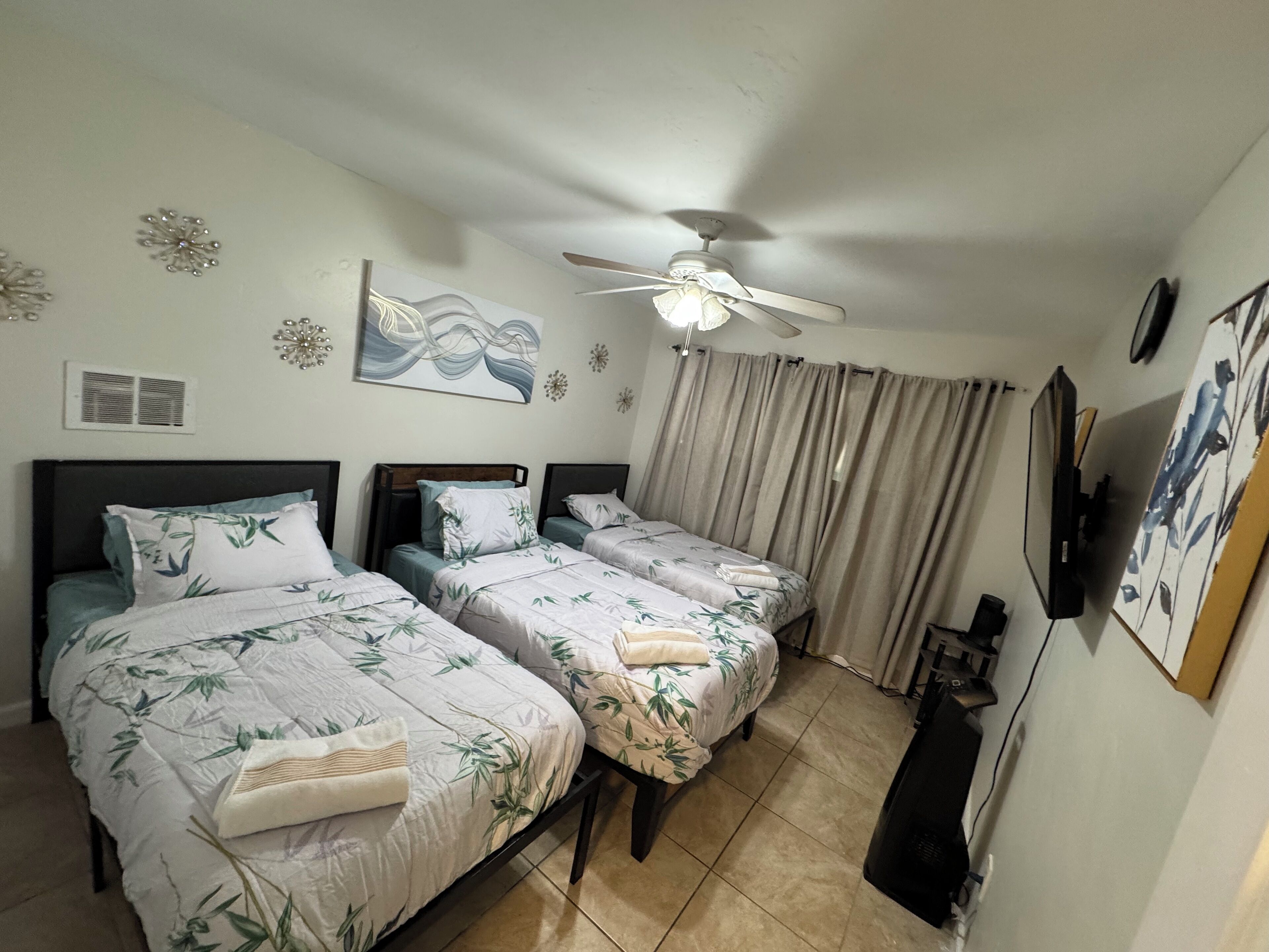 A hotel room with two single beds, a ceiling fan, a TV, and a painting on the wall.
