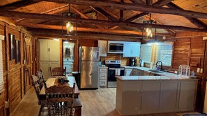 Una cocina rústica con vigas de madera, una isla central y un comedor con mesa y sillas de madera.