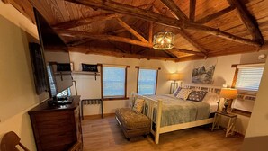 Un dormitorio acogedor con techo de madera, una cama con ropa de cama estampada, un escritorio con una computadora y una silla.
