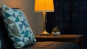 Una cama con un almohadón estampado con motivos geométricos, una mesita de noche con una lámpara y una pequeña planta en maceta.