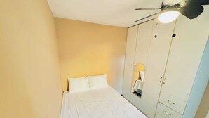 Un dormitorio con cama, armario y ventilador de techo.