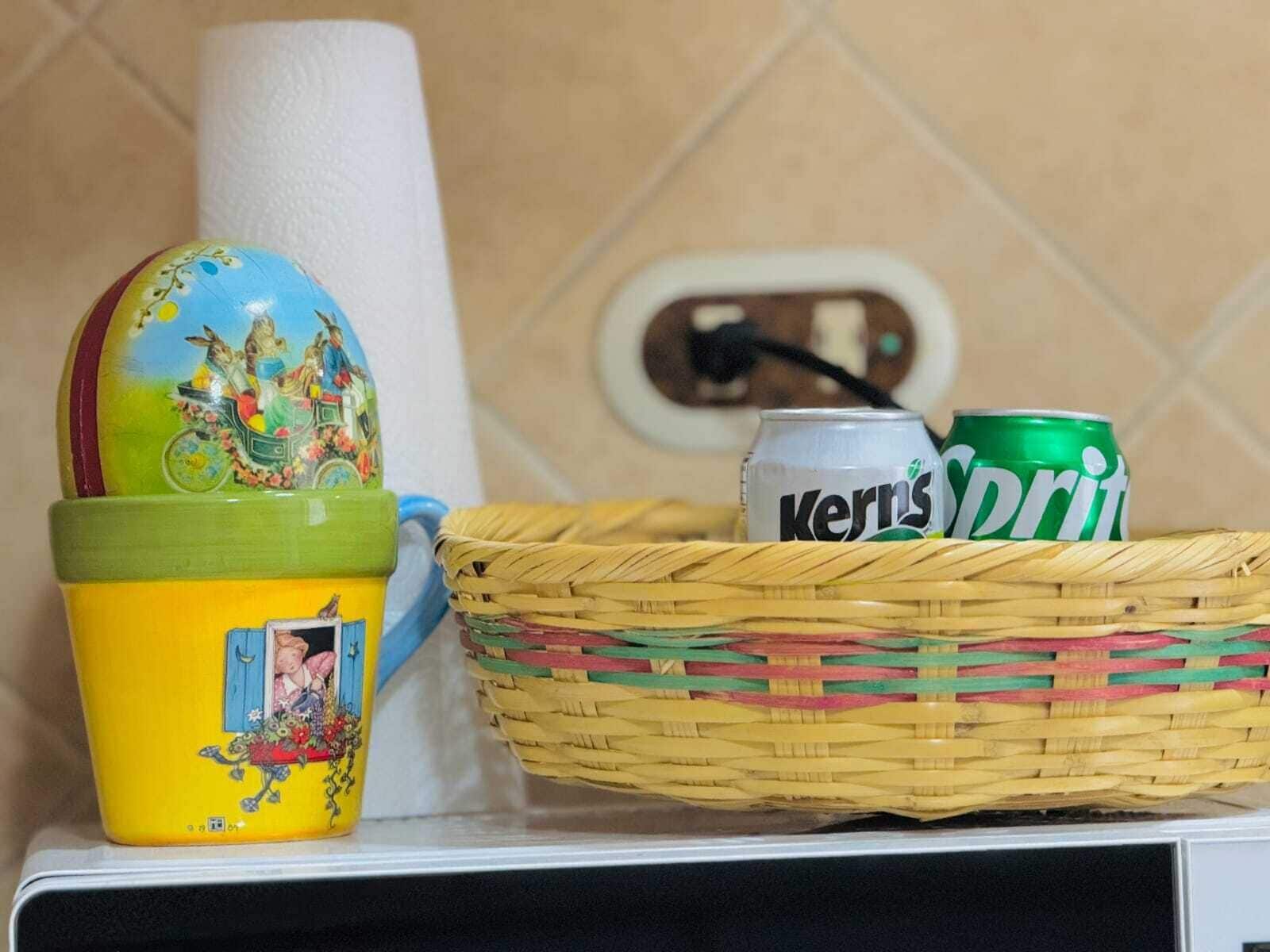 Una encimera de cocina con una taza de cerámica colorida, una cesta de mimbre que contiene una lata de Sprite y un rollo de toallas de papel.