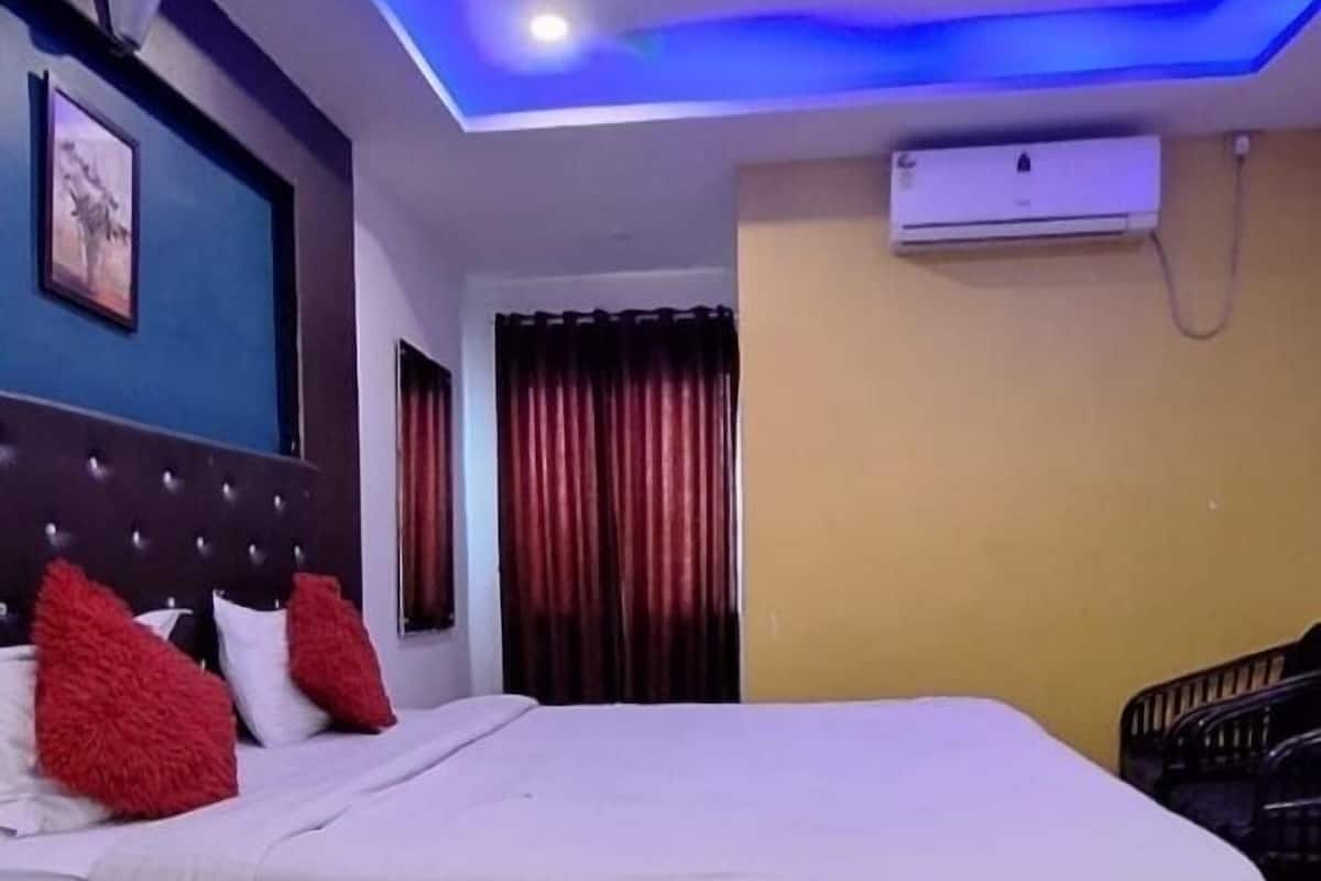 Habitación de hotel con cama, ventilador de techo, equipo de aire acondicionado y ventana con cortinas.
