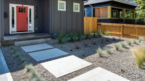 Uma casa moderna com uma porta vermelha, um deck de madeira e um jardim de cascalho com pedras no caminho.
