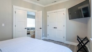 Quarto com uma cama grande, duas portas brancas, uma TV fixada na parede e um escorredor preto pequeno.