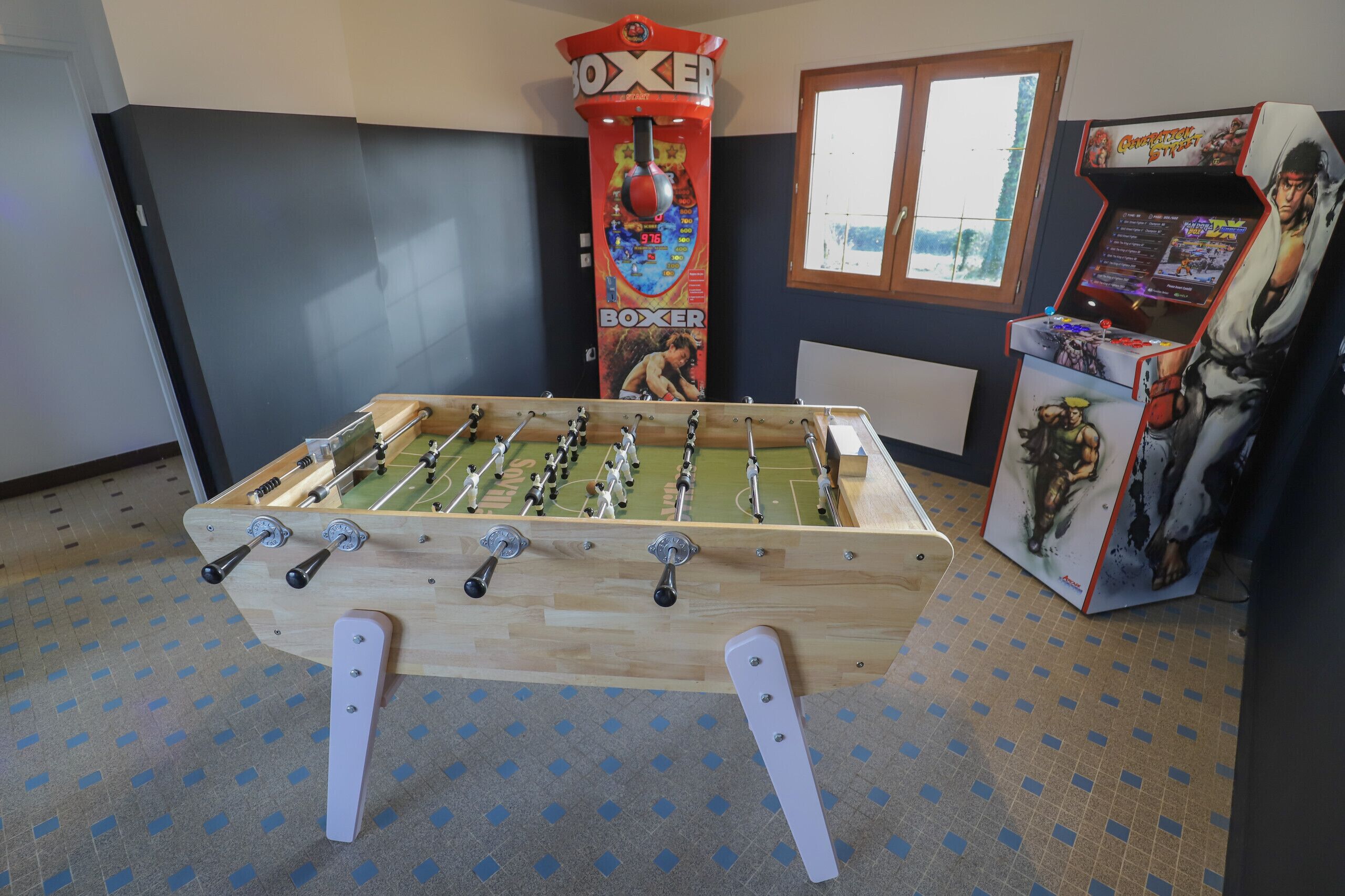 Ein Kicker steht in einem Raum mit Fenster und Spielautomaten.