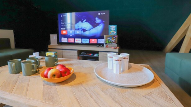 A cozy living room with a TV displaying a movie, a bowl of apples, and a tray with cups.