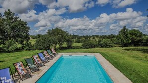 A rectangular swimming pool with a tiled edge, surrounded by a grassy area with trees.