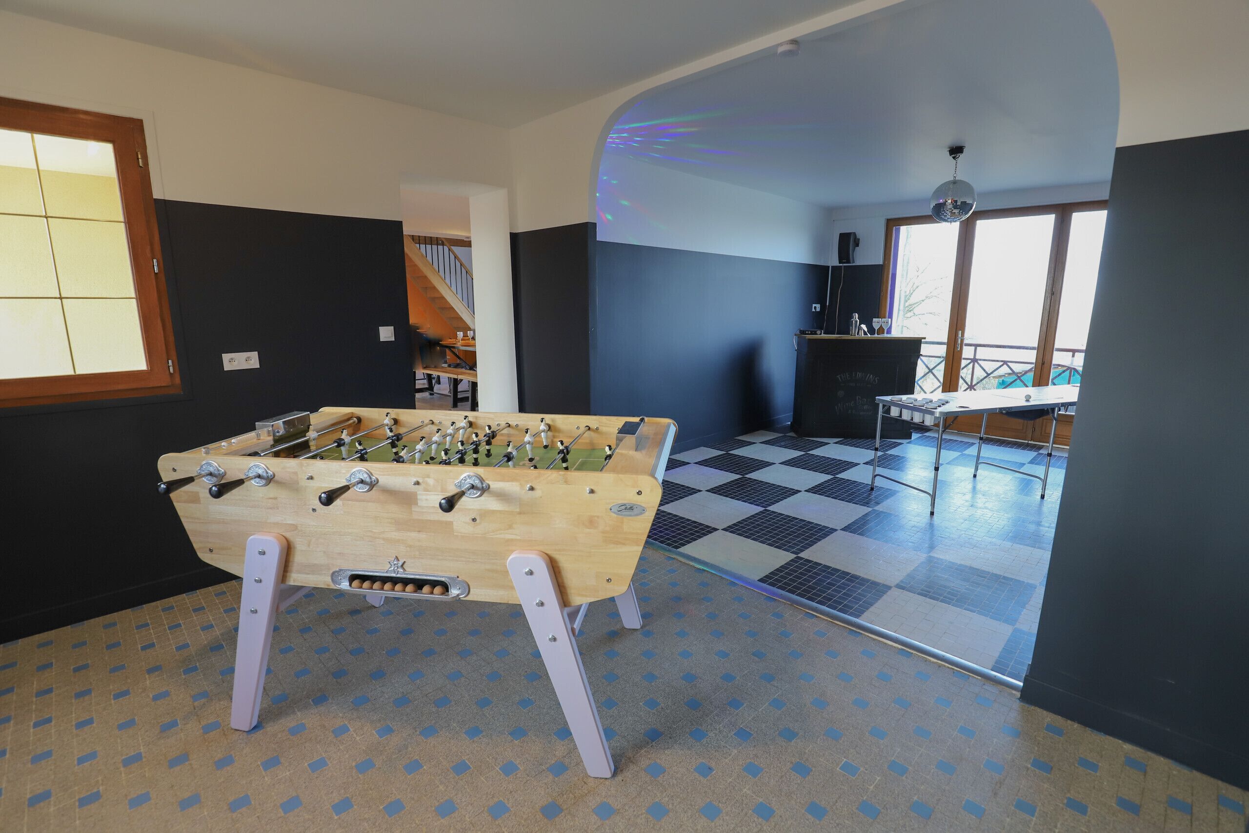 Une pièce avec une table de baby-foot, un sol à carreaux et une vue sur l’extérieur grâce à une grande fenêtre.