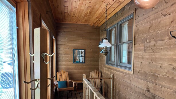A wooden cabin with a porch, a wooden chair, a table, and a hanging lamp. - Cozy Lake view 3-bedroom house WiFi, AC in Oshkosh-Great spaces inside & out EAA (Oshkosh)