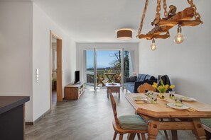 Moderni olohuone, jossa on ruokailutila, suuret ikkunat ja katosta roikkuva valaisin.
