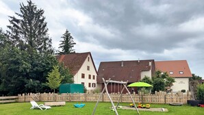 Un pati enjardinat amb un tobogan, una tanca de fusta i una casa amb teulada vermella.