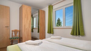 Habitació amb dos llits, un armari de fusta, una cadira i una finestra amb cortines.