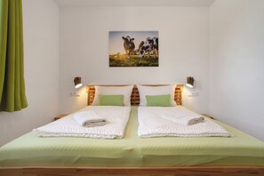 Cama de casal com roupa de cama verde, duas almofadas, quadro de vacas na parede e abajures.
