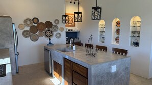 Una cocina moderna con una isla central, luces colgantes y platos decorativos tejidos en la pared.